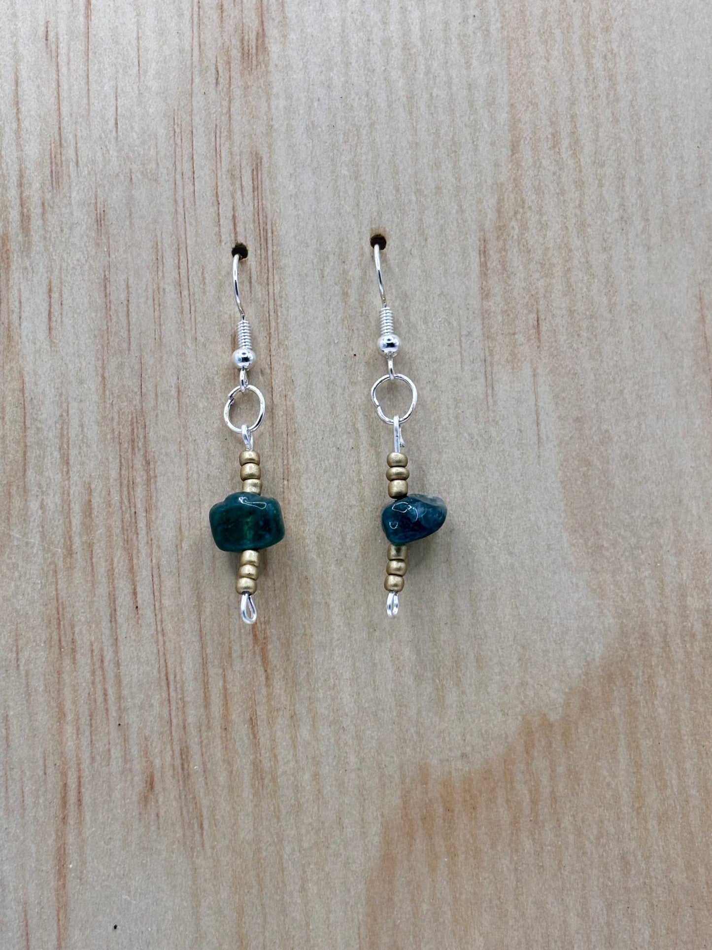 Pair of earrings with green stones on a wooden surface