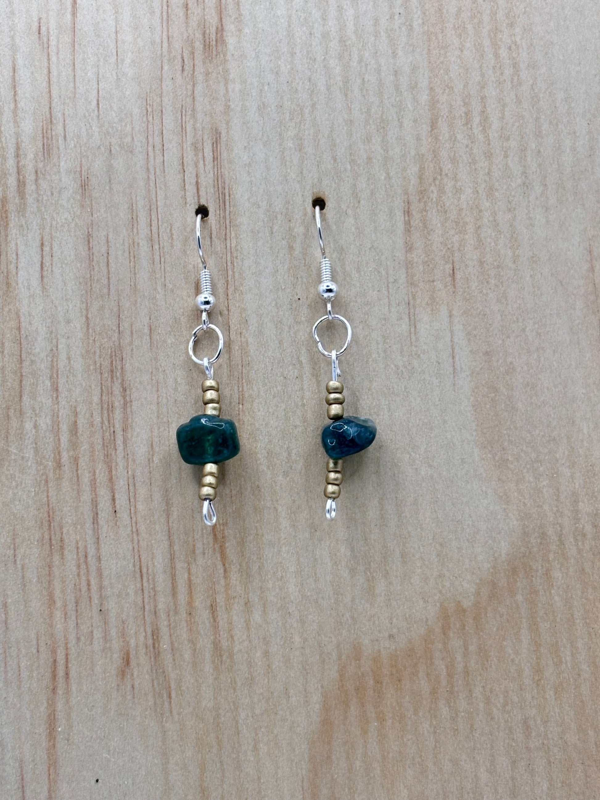 Pair of earrings with green stones on a wooden surface